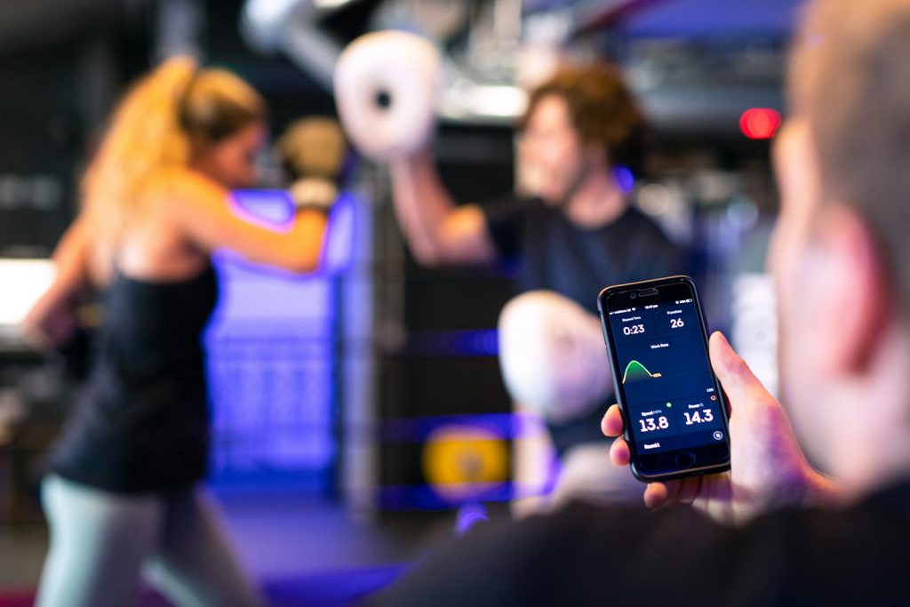 A woman boxing with a trainer while a fitness app tracks performance on a smartphone.